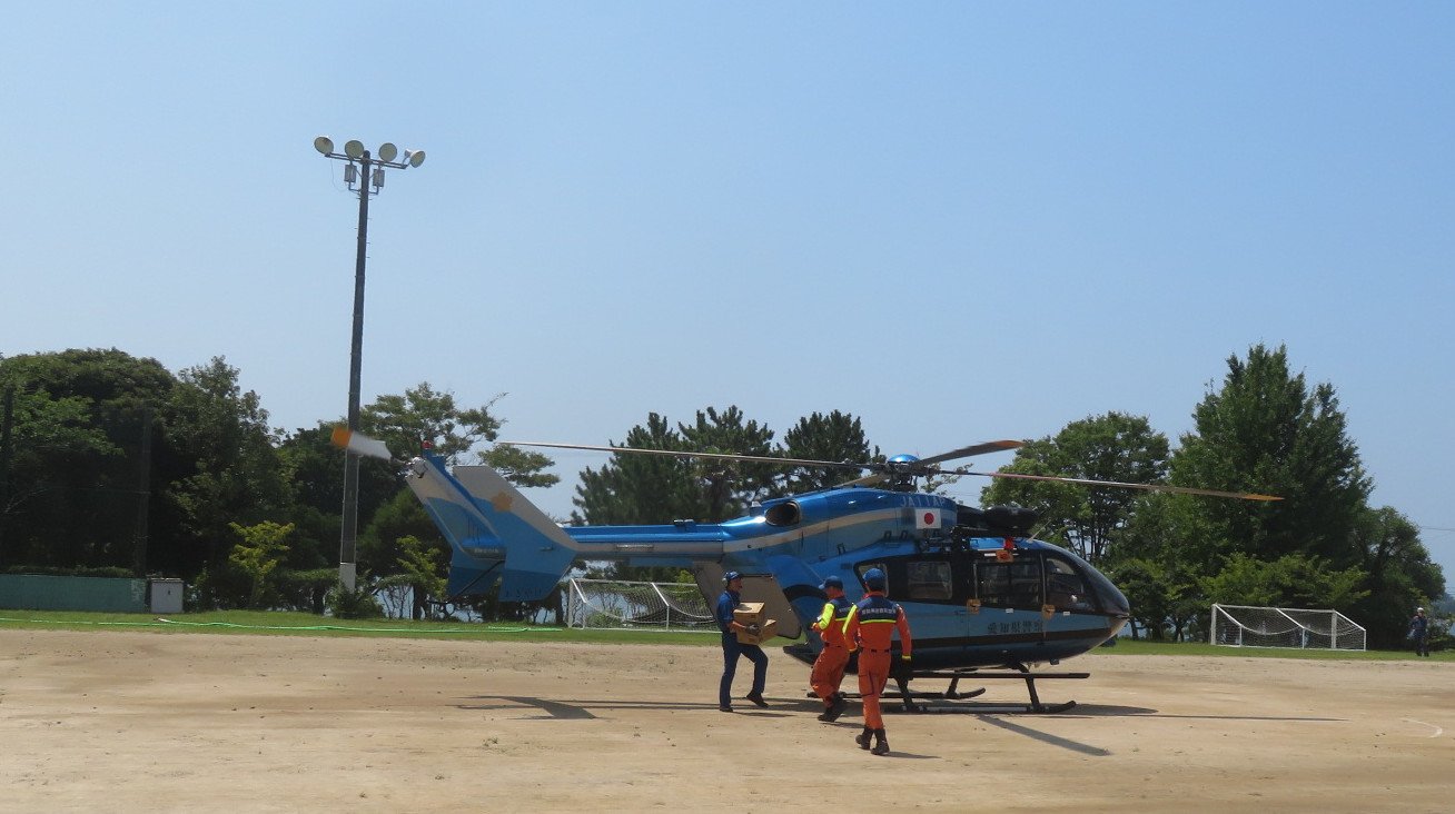 愛知県警のヘリが着陸する瞬間と救援物資の受け渡しの写真