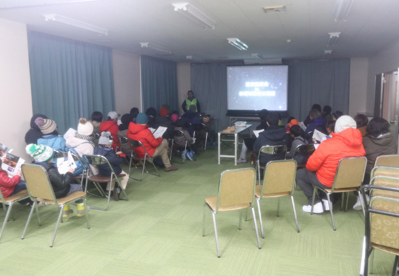 屋内で星空についてスライドを用いて解説する様子