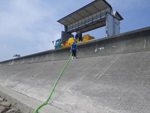 堤防に停車したトラックの水槽から放流用のホースを干潟に延ばしている状況