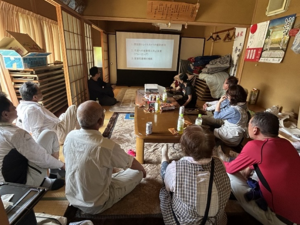 寄り合い所の一室でプロジェクターに映された資料に注目する参加者の様子